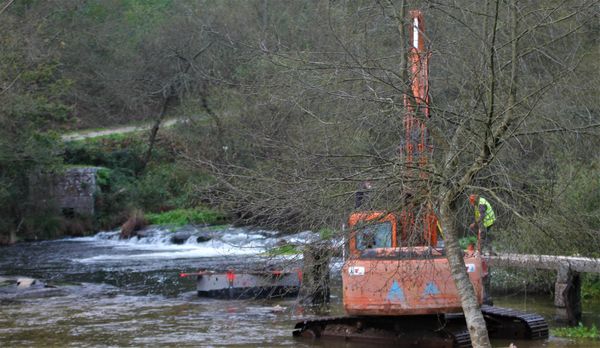 obras: máquina e trabalhadores a erguer pilar de ponte de pedra no rio