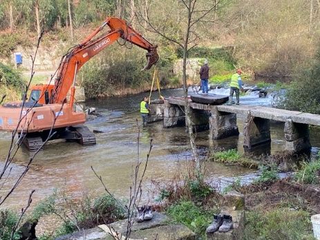 obras: máquina e trabalhadores a erguer pilar de ponte de pedra no rio